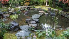 a small pond surrounded by rocks in a garden with lots of trees and bushes around it