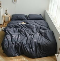 an unmade bed with blue sheets and pillows in a room next to a window