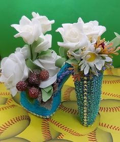 two vases filled with flowers sitting on top of a baseball tablecloth covered table