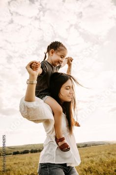 a woman carrying a child on her back in the middle of a field with grass