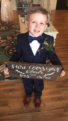 a little boy in a tuxedo holding a wooden sign that says love grows