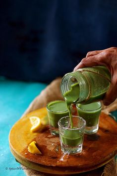 a person pours green liquid into glasses on a wooden tray with lemon wedges