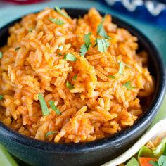 mexican rice in a black bowl with tortillas and cilantro on the side