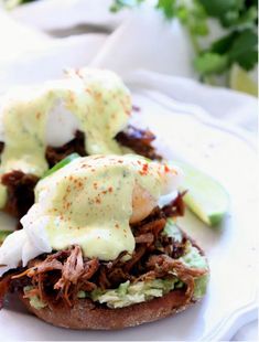 a pulled pork sandwich topped with sour cream sauce and cucumber on a white plate