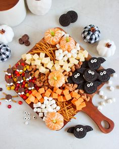 an assortment of halloween treats on a cutting board next to pumpkins, cookies and candies