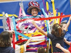 a group of children standing around a woman in a costume made out of strips of paper