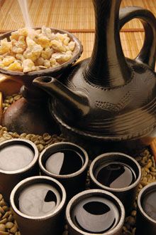 an assortment of coffee cups and teapots on a table with beans in the foreground