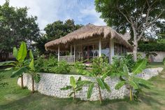 a thatched roof gazebo surrounded by lush green plants and trees on a sunny day