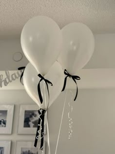 three white balloons with black ribbon tied to them hanging from the ceiling in a room