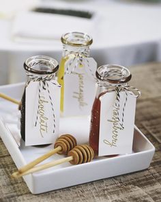 three jars filled with honey sitting on top of a white tray next to a wooden stick