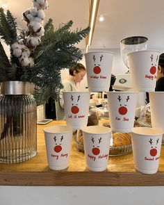 many cups with reindeer faces on them are sitting on a table next to a vase