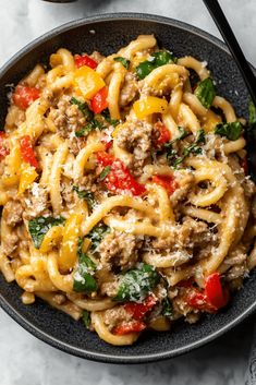 a black bowl filled with pasta and meat on top of a white table next to a fork