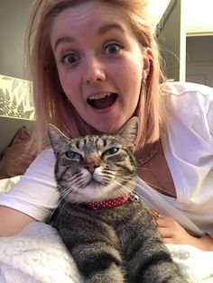 a woman holding a cat in her arms and making a funny face at the camera