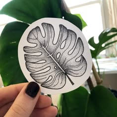 a person holding up a sticker with a leaf on it in front of a potted plant