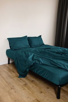 a bed with green sheets and pillows in a room next to a window on a hard wood floor