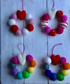 four different colored pom poms are hanging on a white wooden board with string