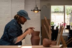 a man in a blue shirt and hat working on a clay vase with his hands