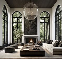 a living room with large windows and a fireplace in the center surrounded by couches