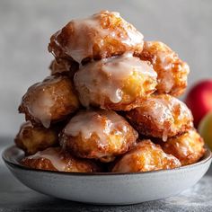 a pile of doughnuts sitting in a bowl next to an apple on the table