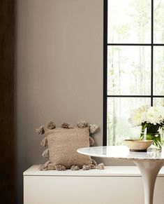 a white table and chair in front of a window with flowers on the bench next to it