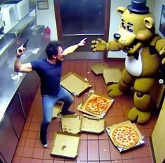 a man standing next to two pizzas on top of cardboard boxes in front of a bear mascot