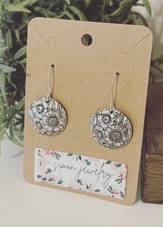 a pair of earrings sitting on top of a wooden box next to a plant in a pot