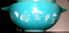 a teal colored bowl with white designs on the front and sides, sitting on a shelf