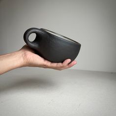 a hand holding a black cup on top of a white table next to a gray wall