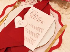 a table setting with red napkins, silverware and a heart - shaped card