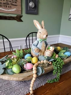 a wooden tray filled with fake eggs and plants on top of a dining room table