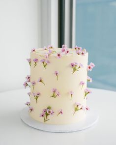 a white cake with pink flowers on it sitting on top of a table next to a window