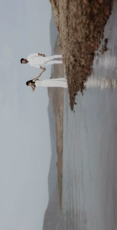 two women in white are standing by the water