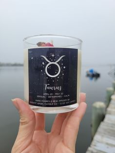 a person holding up a candle with the zodiac sign taurus on it in front of a body of water