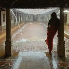 a woman in red sari walking through a water sprinkler covered walkway