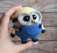 a crocheted minion with big eyes is held up by someone's hand