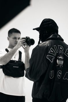 a man in a leather jacket is taking pictures with his cell phone while another man stands behind him