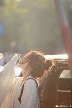 a woman standing next to a car with her hand in her mouth and wearing a white sweater