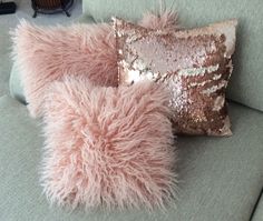 two pink pillows sitting on top of a green couch next to a brown and white pillow