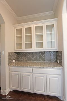 an empty kitchen with white cabinets and marble counter tops, along with hardwood flooring