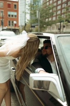 a woman in a white dress getting out of a car with a man standing next to her