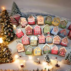 a christmas village with lots of small houses and trees in the snow next to a lit tree