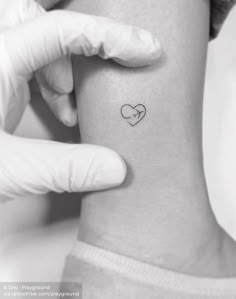 a small heart tattoo on the back of a woman's left arm, which is being held up by a glove