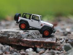 a toy jeep with orange rims is on the ground next to some rocks and grass