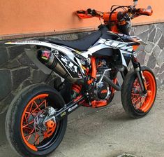 an orange and white dirt bike parked next to a wall