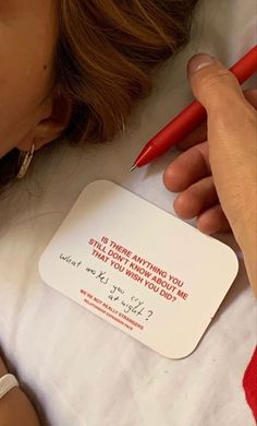 a woman is writing on a card next to a red pen and another person's hand