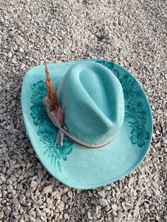 This is a hand burned cowboy hat with details of flowers and foliage. To go with it is has an light pink felt ribbon tied with a brown leather strip of fabric. It is turquoise and it burned to this beautiful dark green/turquoise color.  These custom hand burned wide brim western hats have a unique to the hat fabric hand tied band with feathers and other add ins to make the hat one of a kind. Every hat is customizable free of charge so please feel free to reach out with any customization question and we can make the hat your own!  Hat Details: It is a Cattleman Cowboy Hat in vegan suede. Classic cattleman crown shape. Brim is slightly upturned on the sides. Crown size: 57 cm. Adjustable sizing, hook-and-loop tab inside sweatband. Please allow up to 2 weeks to receive your hat! Teal Cowgirl Hat, Western Green Hat Band For Festivals, Western Green Hat Bands For Festival, Green Western Style Hat Band For Festivals, Green Western Hat Bands For Kentucky Derby, Western Green Hat Bands For Kentucky Derby, Western Green Hat For Country Events, Turquoise Western Fedora With Short Brim, Western Turquoise Brimmed Fedora