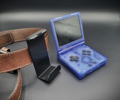 an electronic device is sitting next to a leather belt and case on a gray surface