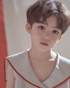 a young boy with brown hair wearing a white shirt and orange trim around his neck