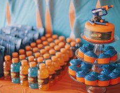 an assortment of blue and orange cupcakes on a table with candy in bottles