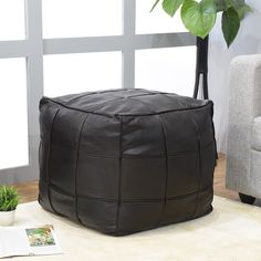 a large square leather ottoman sitting on top of a white rug next to a chair